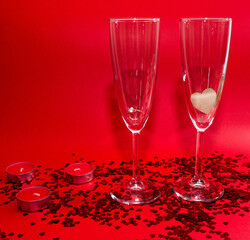 Romantic evening. Glasses of champagne, red candles, red confetti in the shape of a heart on a red background