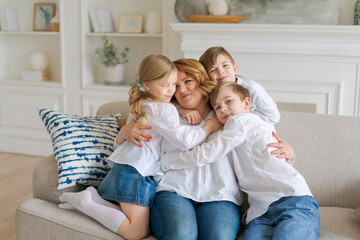 Cute kids hugging, excited mom showing love and affection, smiling mother and daughter and two school-age sons having fun at home, hugging sharing intimate tender moment together