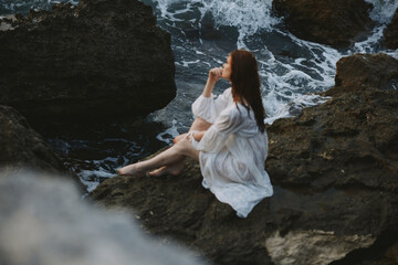 Woman in white wedding dress barefoot sitting on a stone nature