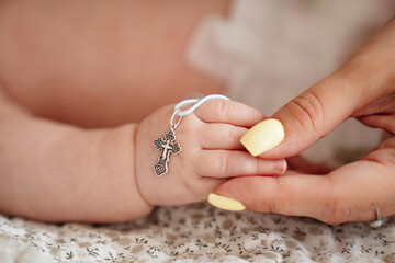 mother's hand holds the hand of a baby with an Orthodox cross.
