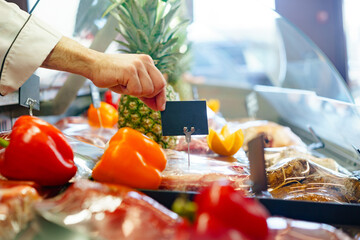 Male hand putting price tag on display of meat in shop, copy space