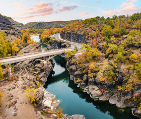 Aerial drone view of a road passing a narrow gorge of a river by bridge during golden autumn in Greece