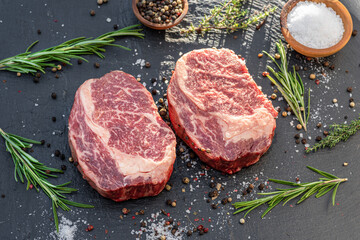 Raw Ribeye steaks with salt and herbs on grey board. Top view.