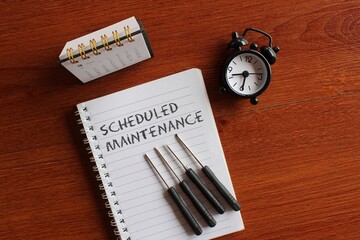 Top view image of calendar, alarm clock, screwdriver and book with text SCHEDULED MAINTENANCE.