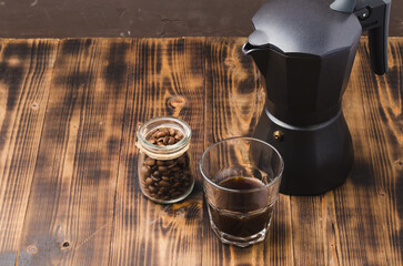 Glass of cofee with coffee beans. Top view. Сup of black coffee in a glass and grains in a glass jar with a coffee maker on a wooden table.
