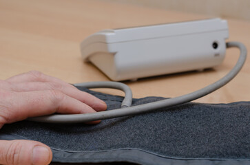 Male hand and Digital blood pressure monitor on brown table. Che