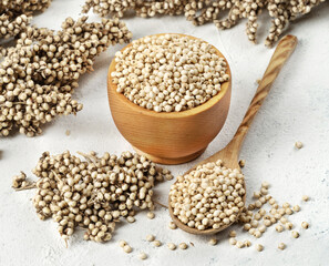 White sorghum seeds in a wooden bowl with a spoon on a light background.