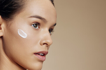 portrait woman cream on cheek posing cosmetics to clean skin beige background