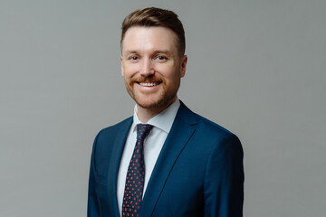 Cheerful male CEO in suit smiling at camera while posing against grey background