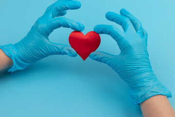 Obraz premium Red heart in hands in blue medical gloves on blue background. Background for the day of the medic. World Heart Day. Heart diseases.