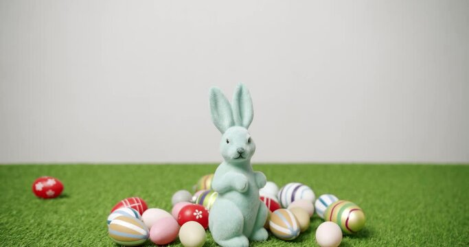 Rabbit toy on a isolated background of green grass with many colored eggs. Place for Text. Cute fluffy rabbit, Lovely Animal concept. Happy Easter day. Banner for Easter Design Concept. Bunny Toy.
