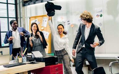 Young diverse and multiracial businesspeople wearing formal suits, singing, dancing together, laughing with happiness and fun while working in indoor modern office or company.