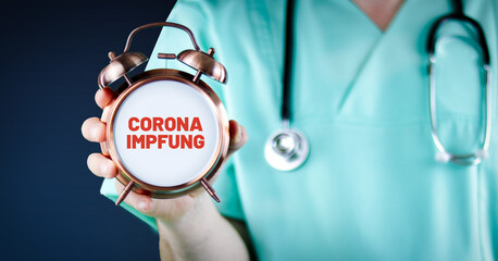 Corona-Impfung. Arzt zeigt Wecker/Uhr mit Text. Hintergrund blau.