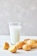 Potato milk in a glass mug stands on the table next to fresh potato tubers. Alternative plant based...