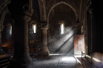 Stone interior with arch and column of Ancient Armenian church in the highlands. Dark hall and rays...