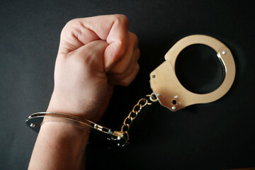 hands clenched into fists in handcuffs in the form of chains on a black background, the problem of...