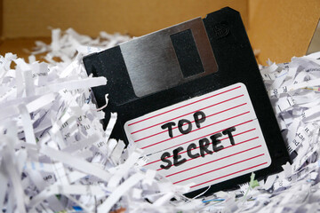 Top secret information on retro vintage floppy disk magnetic computer among shredder paper, thief...