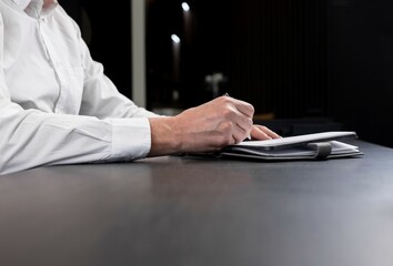 Businessman opened planner and is taking work notes or writing agenda. Man hands closeup. . High quality photo