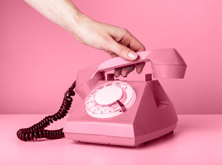 Woman hand holding retro phone handset on pink background and answering to call or hanging up. High quality photo