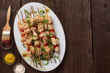 Meat kebabs on a large platter with sauces and herbs, wooden background with copy space