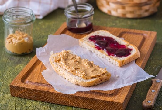 Snack or lunch, sandwiches on white bread with peanut butter and jam on a wooden board on a green concrete background. Classic sandwich recipes.