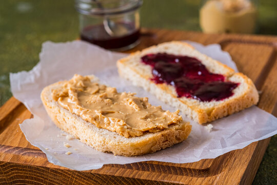Snack or lunch, sandwiches on white bread with peanut butter and jam on a wooden board on a green concrete background. Classic sandwich recipes.