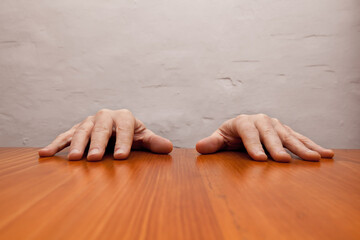 Men's hands resting on the top of a wooden table.