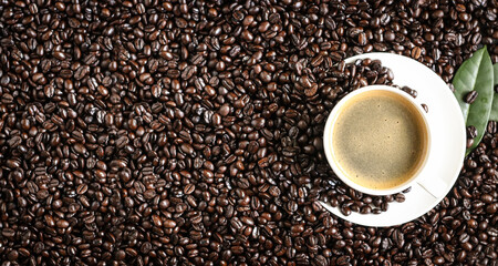 Hot coffee in a white coffee cup and many coffee beans placed around a on dark background.