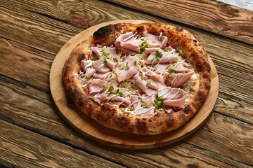 Fresh pizza with ham and pineapple on wooden table in restaurant.