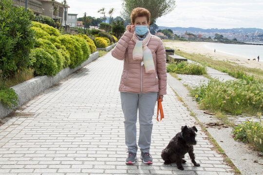 Portrait Of A Senior Woman With A Medical Mask On Her Face In Protection Against The Coronavirus With Her Dog