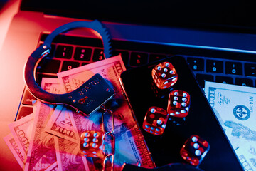 Online casino and law concept. Playing dice, smartphone and handcuffs on keyboard in neon light