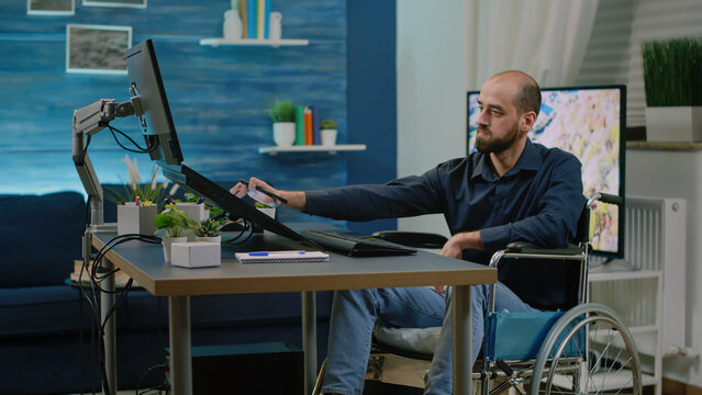 Disabled photographer editing pictures in photography studio. Man with handicap working as editor and retouching photos with graphic tablet and software while sitting in wheelchair.