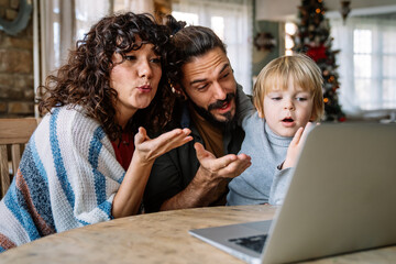 Happy young family making video call with laptop at home