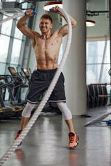 Plakat Front view of Attractive young fit and toned sportswoman working out with battle ropes. Motion blur