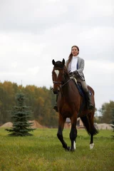 Foto op Canvas Beautiful young woman riding a horse on the field. Sideways to the camera. Freedom, joy, movement © Georgii