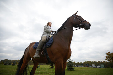 Beautiful young woman riding a horse on the field. Sideways to the camera. Freedom, joy, movement