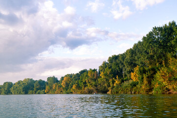 Obraz premium Woman in kayak paddle in autumnal Danube river on a calm autumn morning. Landscape with a kayak on a background of yellow and green autumn trees