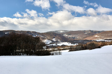 Winter mountain snowy landscape with forest. Beautiful blue sky with white cluster of clouds. Hills in the background. Nature background, wallpaper. Protected area Vrsatec, Slovakia.