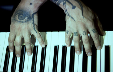 Tattooed mans hands on the keyboard of a piano