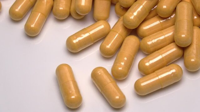 Closeup of many yellow medical capsules, vitamin supplement rushing on a white plate. Medicine and dietary supplements. 4K