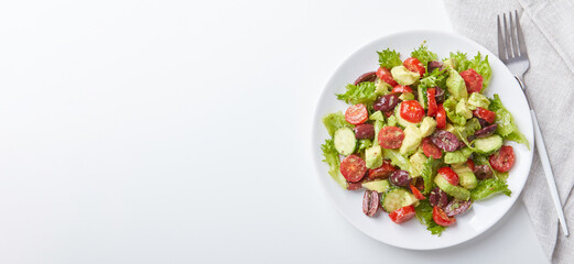 Salad with lettuce, cucumbers, tomatoes, olives and avocados in white plate on the table