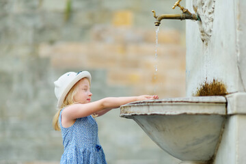 Young girl playing in drinking water fountain in Lucca city, known for its intact Renaissance-era city walls and well preserved historic center. Tuscany, Italy. - obrazy, fototapety, plakaty