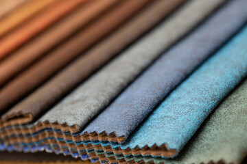 Fabric swatches in different colors are stacked for selection. A variety of shades of upholstery material for furniture and interior. Fabric texture close up. A set of multi-colored rolls of material.