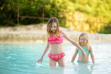 Fototapeta na wymiar Two young sisters bathing in natural swimming pool in Bagno Vignoni, with thermal spring water and waterfall. Tuscany, Italy.