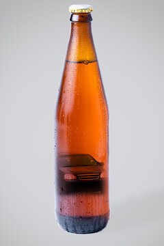 Wet bottle of dark beer with a picture of a car inside. Gray background, vertical orientation. The concept of drunk driving and alcoholism