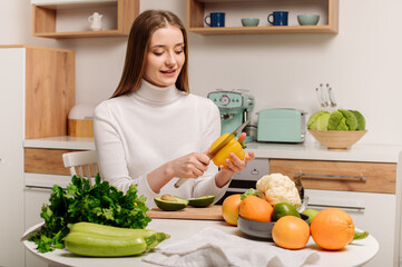 A young, beautiful vegetarian girl or blogger prepares breakfast of fruits, vegetables and greens at home in the kitchen. Blog about healthy eating
