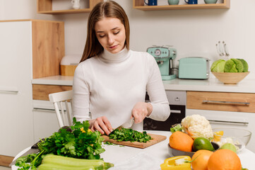 A young, beautiful vegetarian girl or blogger prepares breakfast of fruits, vegetables and greens at home in the kitchen. Blog about healthy eating
