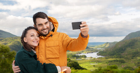 technology, travel and travel concept - happy couple with smartphone over river valley at Killarney...