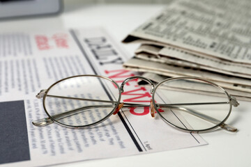 Stack of newspapers and glasses on white table, closeup