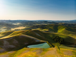 Fototapeta premium Stunning aerial view of green fields and farmlands with small villages on the horizon. Rural landscape of rolling hills, curved roads and cypresses of Tuscany, Italy.